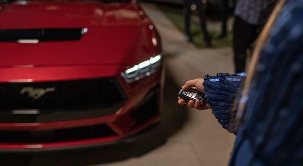 A close-up of a person pointing their keys at the face of a red 2024 Ford Mustang.