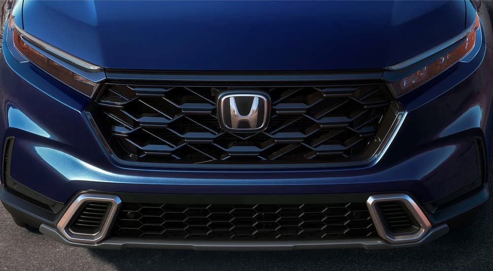 The grille and badge of a blue 2023 Honda CR-V Hybrid is shown.