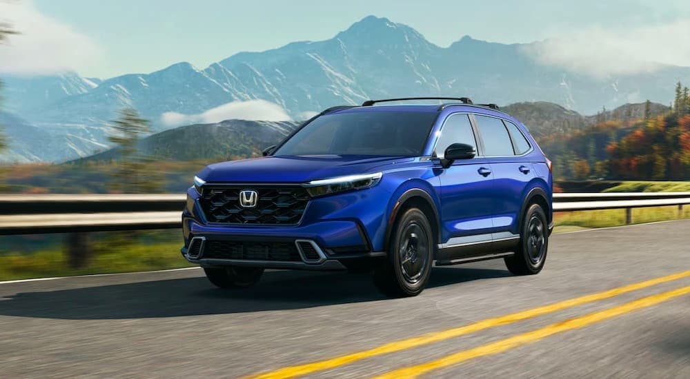 A blue 2023 Honda CR-V Sport Touring Hybrid is shown driving on a highway near mountains.