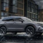 A gray 2023 Honda CR-V Sport Touring Hybrid is shown driving on a wet road after viewing a Honda CR-V for sale.