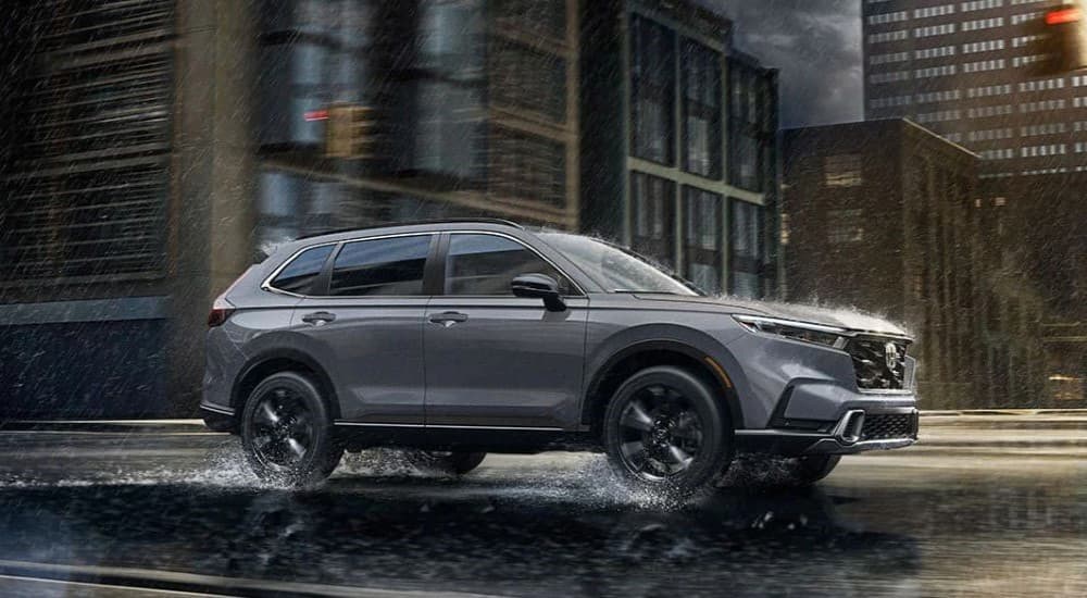 A gray 2023 Honda CR-V Sport Touring Hybrid is shown driving on a wet road after viewing a Honda CR-V for sale.