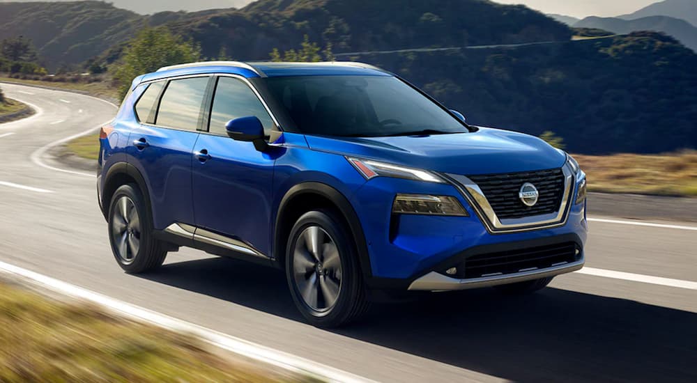 A blue 2021 Nissan Rogue is shown driving on a winding highway.