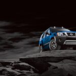 One of the older used SUVs for sale, a blue 2015 Nissan Xterra, is shown parked on a dark rocky cliff.