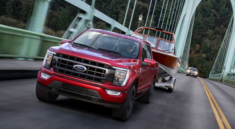A common used truck for sale, a red 2021 Ford F-150, is shown driving on a bridge.