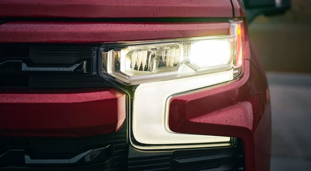 A close-up on the headlight of a red 2023 Chevy Silverado 1500 is shown.