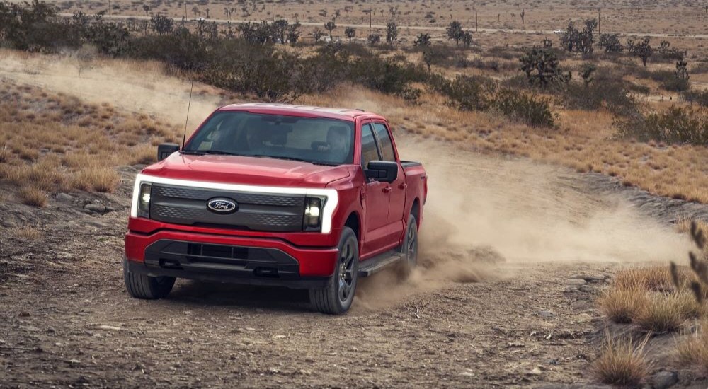 A red 2023 Ford F-150 Lightning is shown driving on a dusty road.