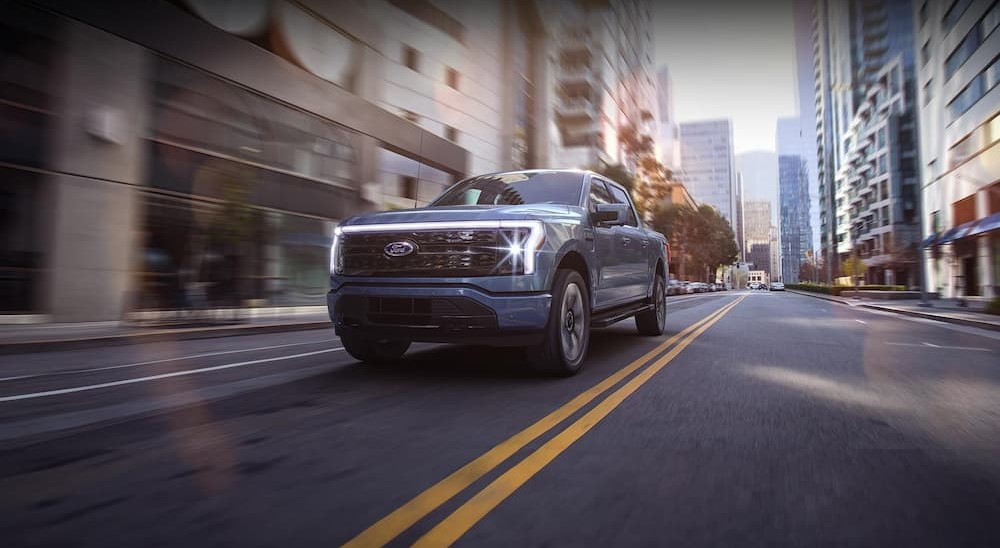 A blue 2023 Ford F-150 Lightning is shown driving on a city street.