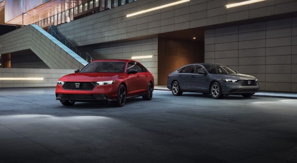 A pair of 2023 Honda Accord Sport L Hybrid LX's are shown parked in a garage, one red and the other grey.