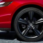 A close-up on the front wheel of a red 2023 Honda Accord Sport L Hybrid, parked for a 2023 Honda Accord vs 2023 Nissan Altima competition, is shown.