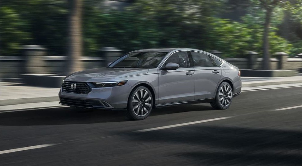 A grey 2023 Honda Accord Touring Hybrid is shown driving down a street with trees in the background.