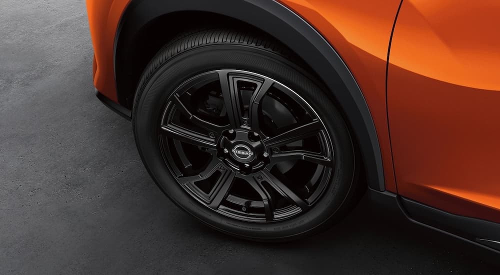 A close-up of a wheel on an orange 2023 Nissan Kicks S is shown.