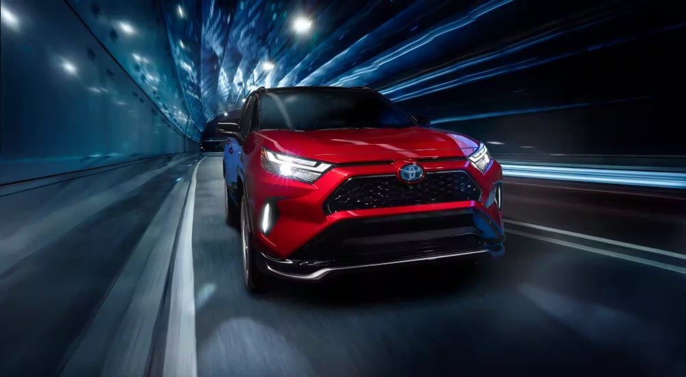 The newest Toyota RAV4 Prime for sale, a red 2023 Toyota RAV4 Prime, is shown driving through a tunnel.