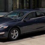 A blue 2024 Chevy Malibu is shown parked on a city street.