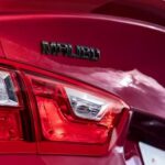 A close-up of a red 2024 Chevy Malibu badge is shown.
