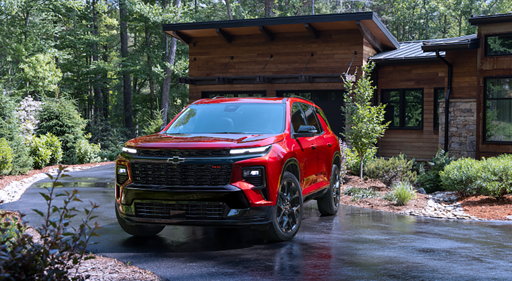 A new Chevy Traverse for sale, a red 2024 Chevy Traverse, is shown parked near a building.