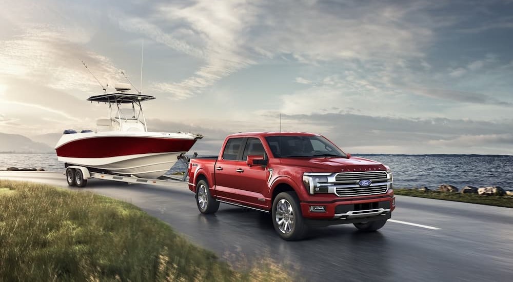 A red 2024 Ford F-150 Platinum is shown towing a boat near a lake.