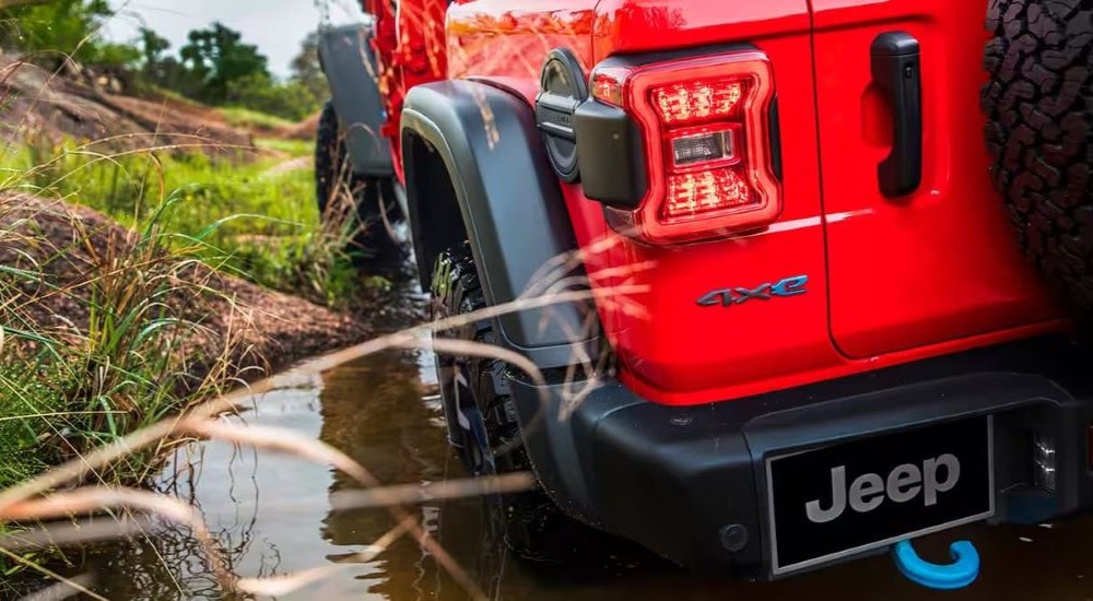 The back wheel of a red 2024 Jeep Wrangler 4xe is shown parked in a marsh.