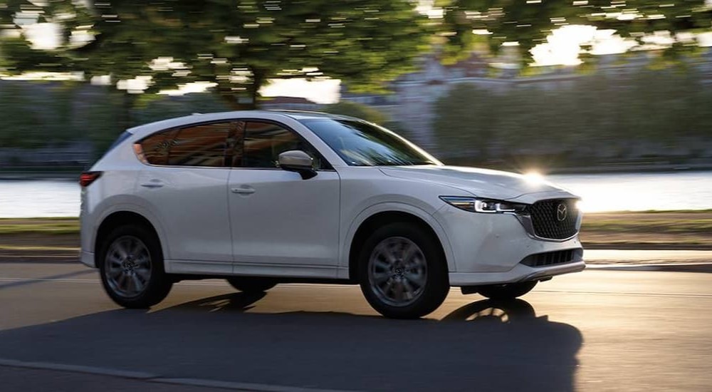 A white 2024 Mazda CX-5 is shown driving near a river.