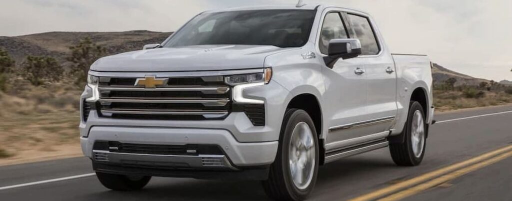 A white 2024 Chevy Silverado 1500 is shown driving on a highway.