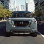 A silver 2024 Nissan Pathfinder is shown driving down a city boulevard.