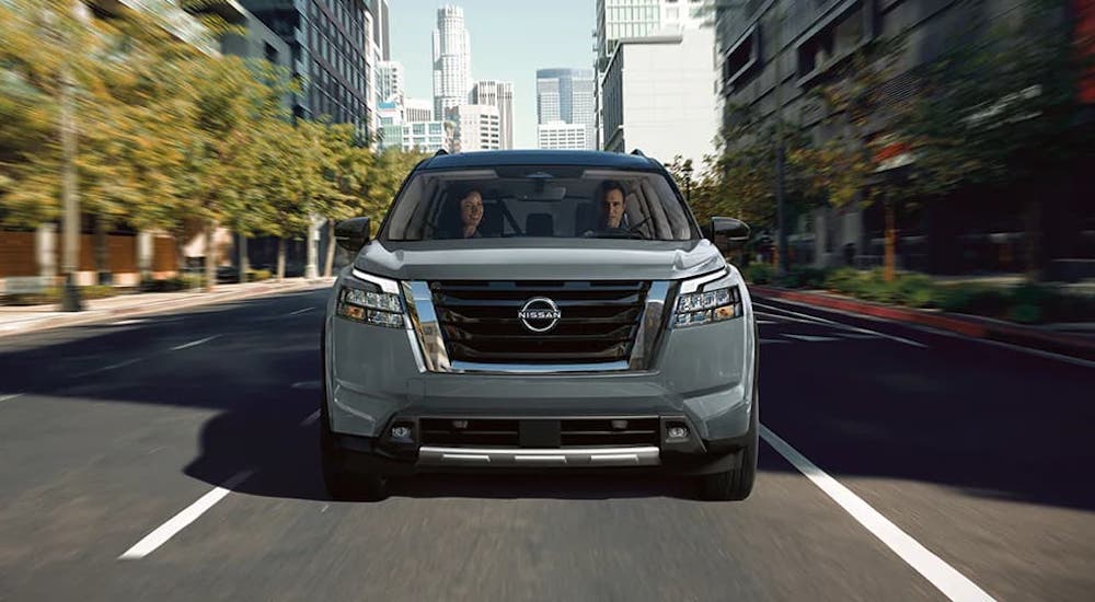 A silver 2024 Nissan Pathfinder is shown driving down a city boulevard.