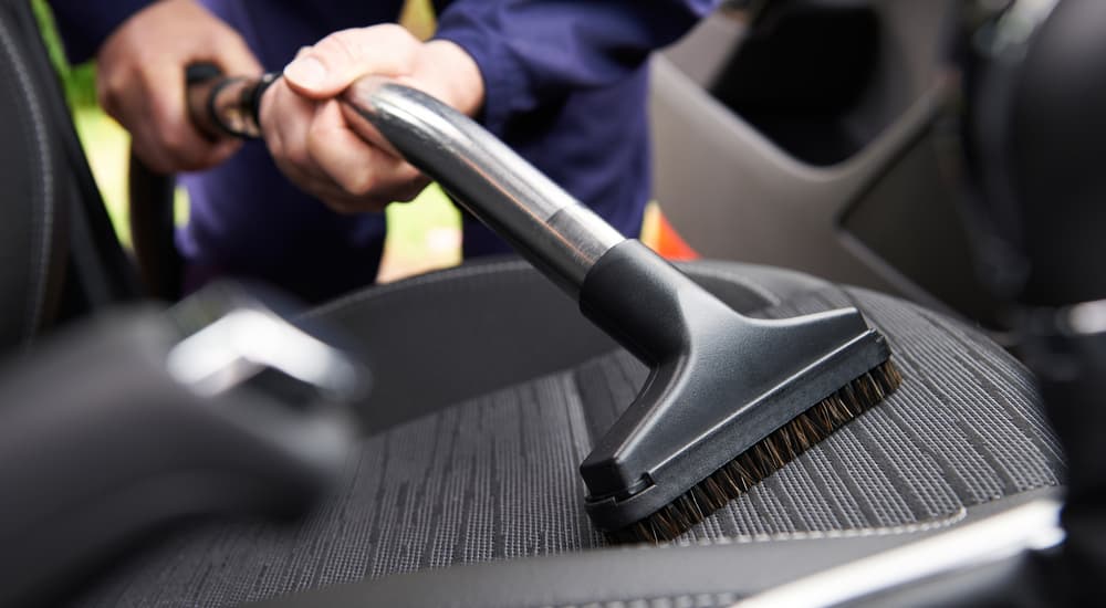 A person is shown vacuuming a car seat.