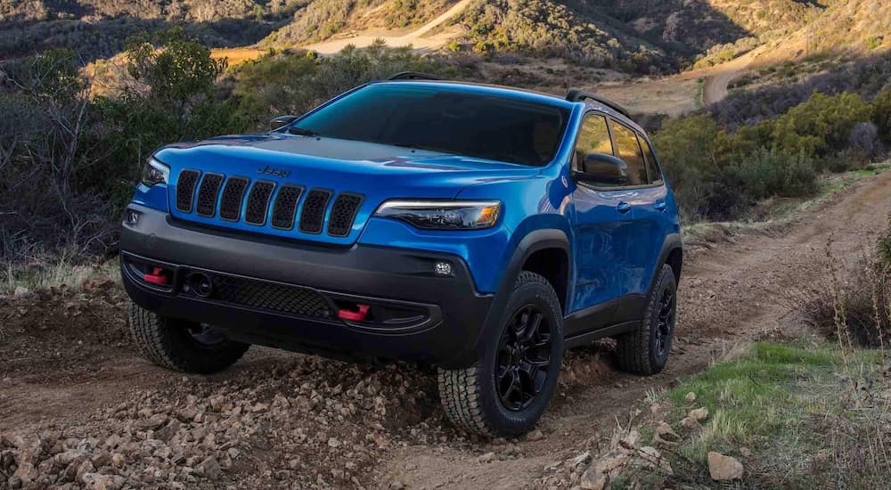 A blue 2023 Jeep Cherokee Trailhawk is shown off-roading on a dirt trail.