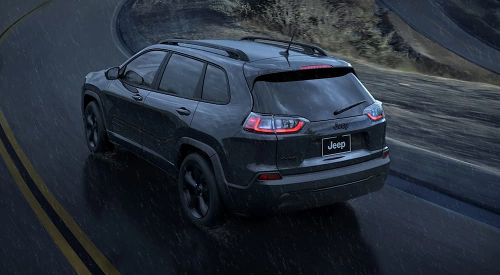 A grey 2023 Jeep Cherokee Altitude LUX is shown from the rear driving in the rain near a Jeep dealer.