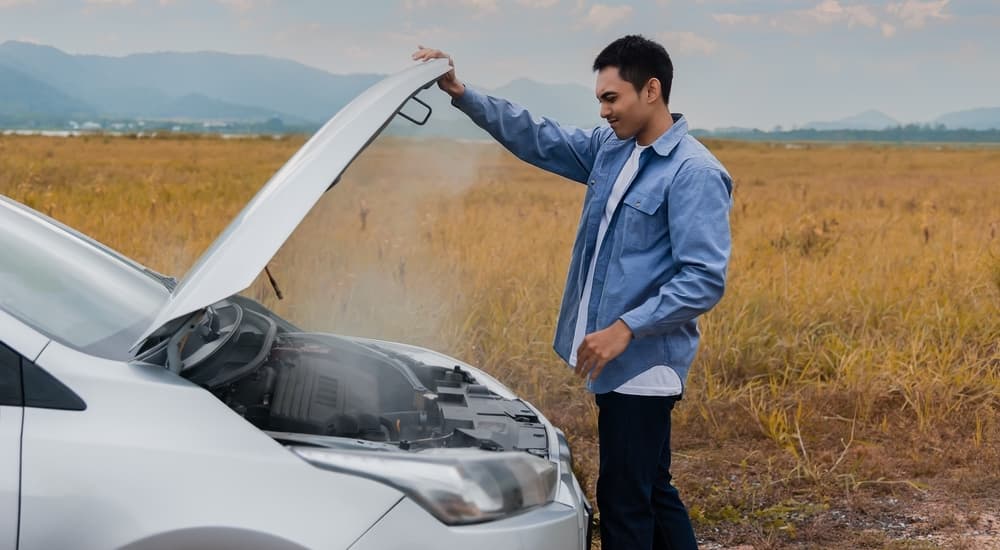 A man is shown looking at the engine of an overheating white car.