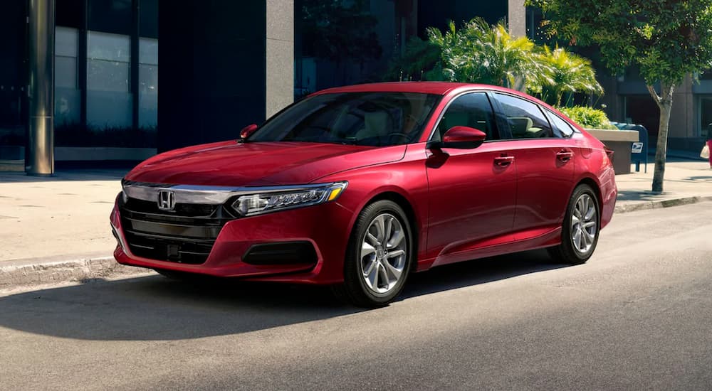 A red 2020 Honda Accord LX is shown driving near a used Honda dealership.