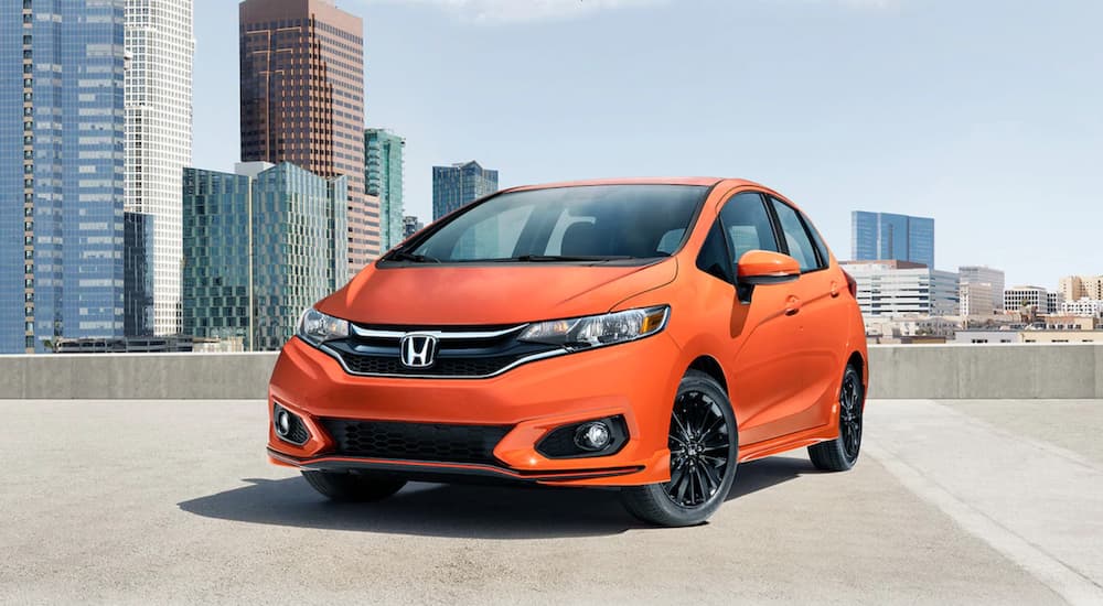 An orange 2020 Honda Fit is shown parked near many city buildings.
