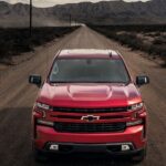 A new Chevy Silverado 1500 for sale, a red 2024 Chevy Silverado 1500 RST, is shown driving on a dirt road.
