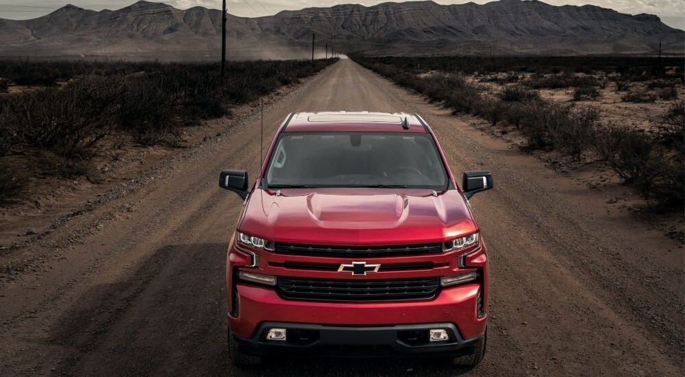 A new Chevy Silverado 1500 for sale, a red 2024 Chevy Silverado 1500 RST, is shown driving on a dirt road.