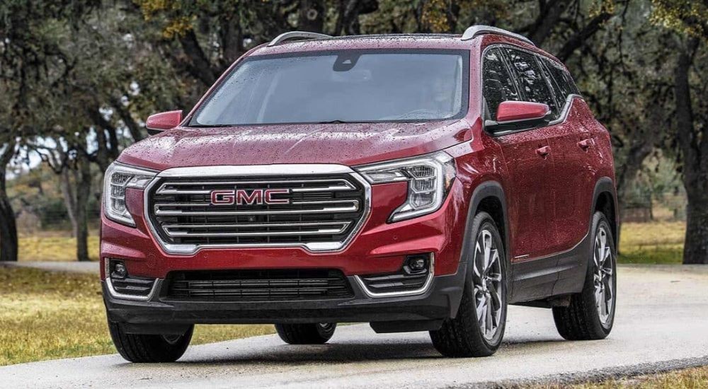 A red 2023 GMC Terrain SLT is shown driving on a trail away from a used GMC dealer.