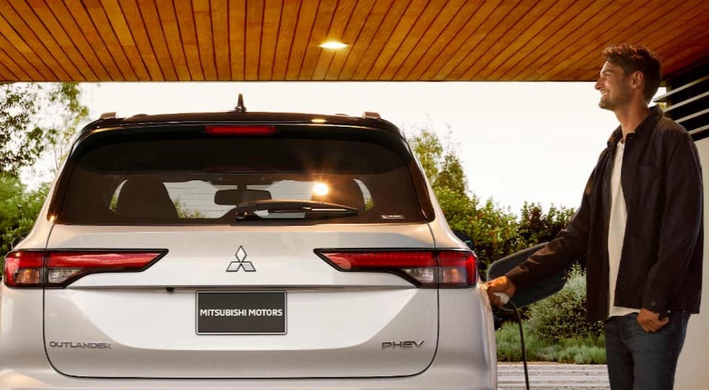 A person is shown charging a white 2023 Mitsubishi Outlander PHEV.