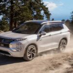 A white 2023 Mitsubishi Outlander PHEV is shown driving off-road looking for EVs for sale.