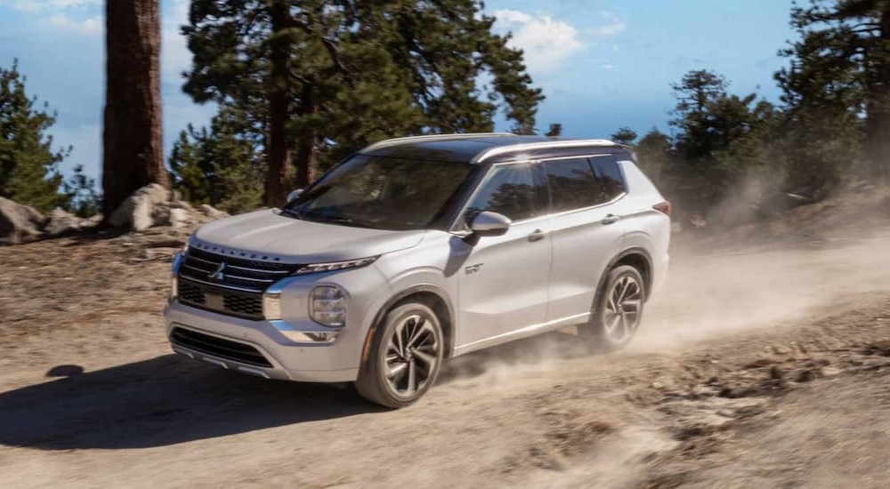 A white 2023 Mitsubishi Outlander PHEV is shown driving off-road looking for EVs for sale.