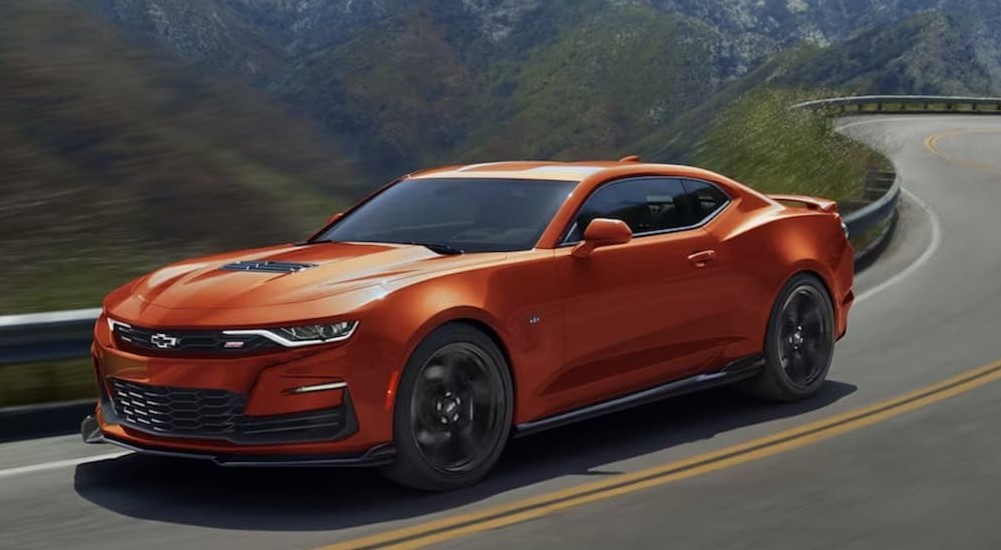 An orange 2024 Chevy Camaro is shown driving on a highway.