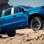 A blue 2024 Chevy Silverado 1500 ZR2 is shown climbing a rocky hill after winning the 2024 Chevy Silverado 1500 vs 2024 Ram 1500 competition.