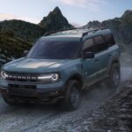 A green 2024 Ford Bronco Sport driving down a dusty hill.