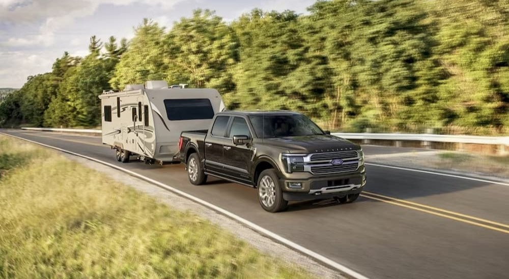 A black 2024 Ford F-150 Platinum is shown driving on a highway towing a camper.