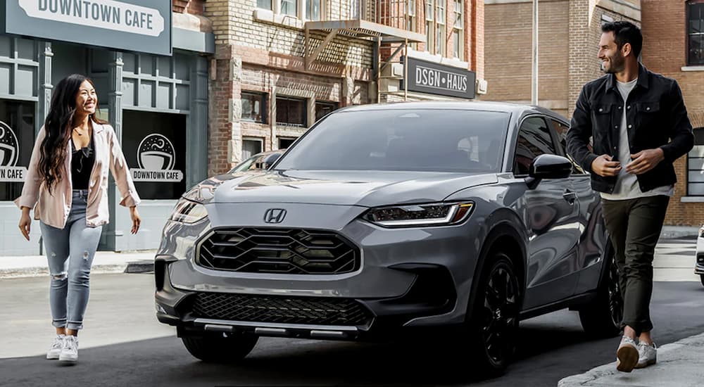 A grey 2024 Honda HR-V is shown parked on a city curb as two people walk away from it.