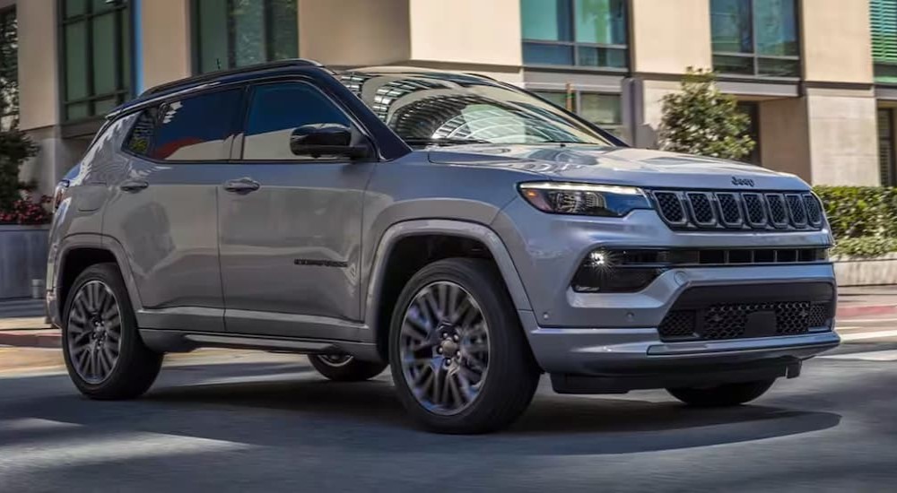 A silver 2024 Jeep Compass is shown driving on a city street.