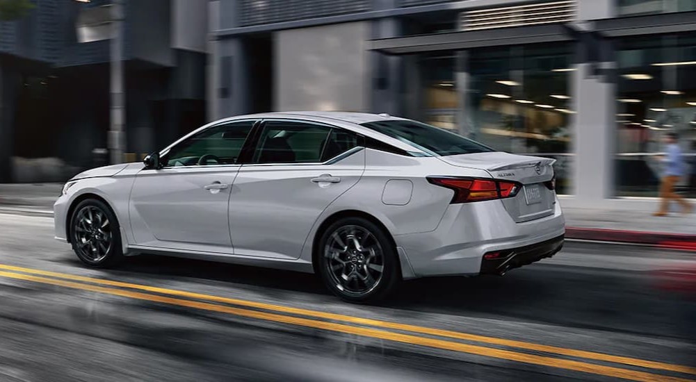 A white 2024 Nissan Altima is shown driving on a city street.