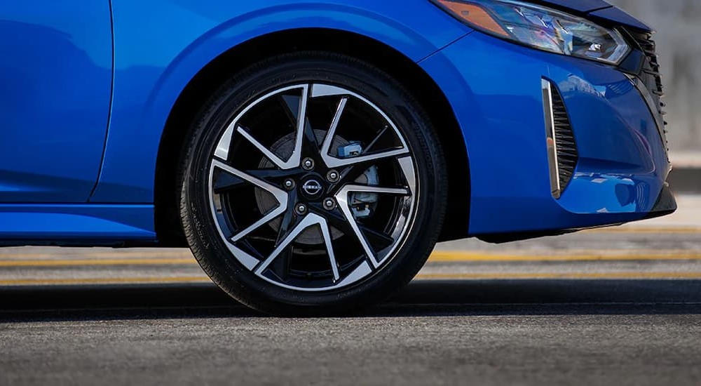 A close-up of a wheel on a blue 2024 Nissan Sentra SR is shown.