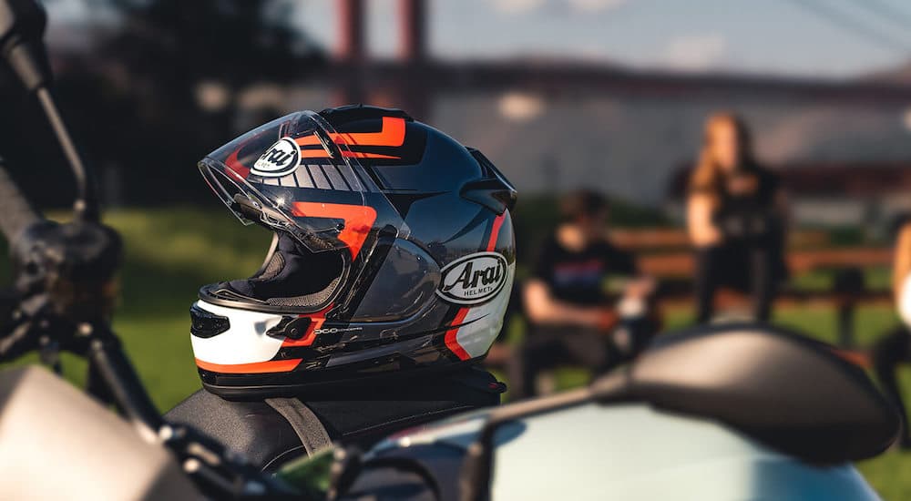 A black-and-orange Arai motorcycle helmet is shown sitting atop a motorcycle at a motorcycle dealership.