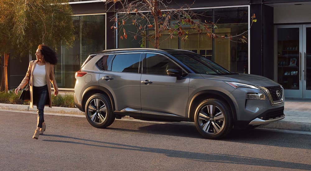 A woman is shown walking away from a grey 2023 Nissan Rogue parked on the side of a street.
