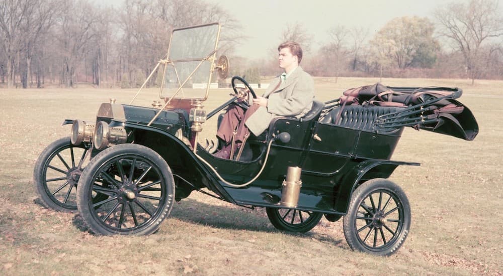 A green 1908 Ford Model T is shown driving uphill on grass.