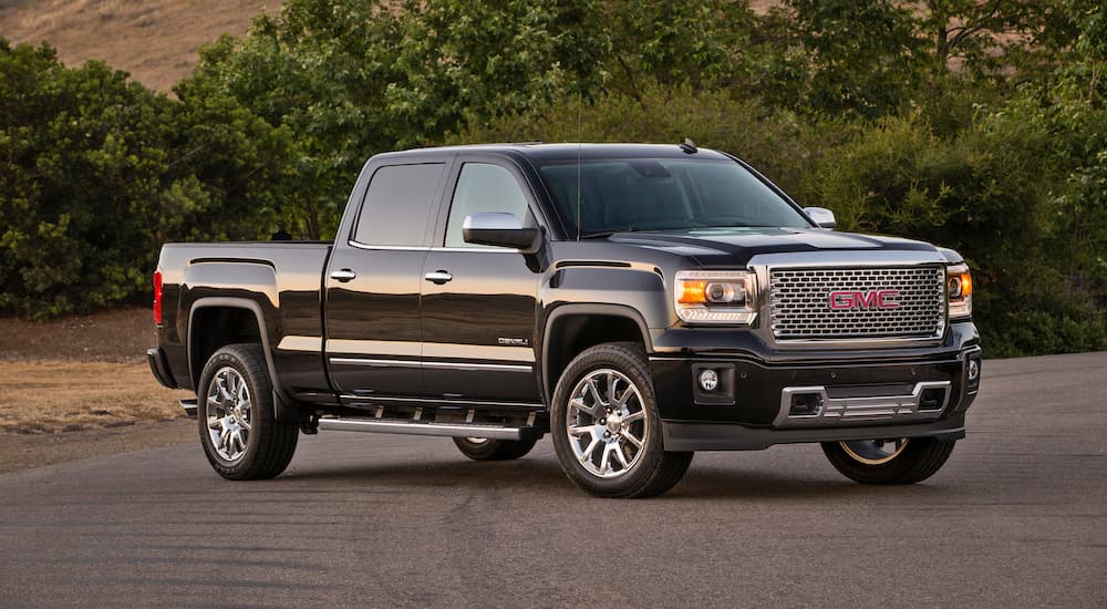 A black 2014 GMC Sierra 1500 Denali is shown parked near a tree-line.