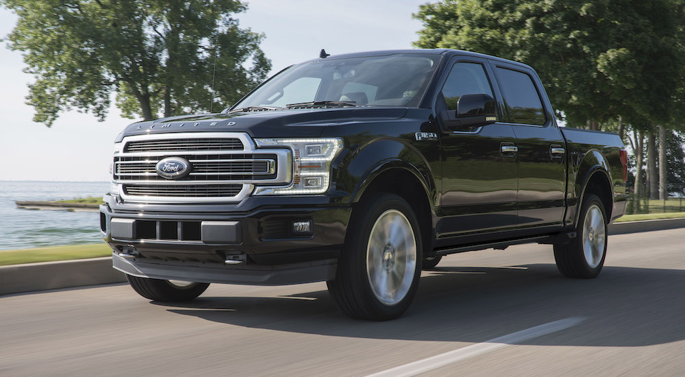 A black 2015 Ford F-150 Platinum is shown driving near water after visiting a Ford dealer.